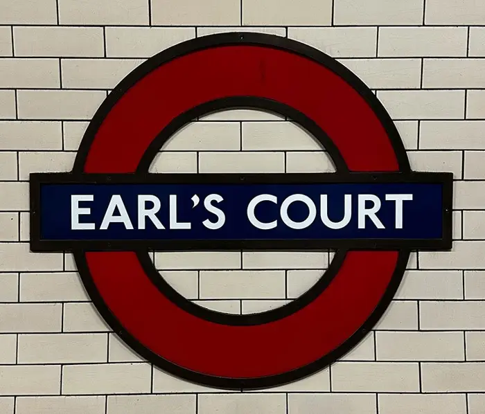 The red and blue Earl’s Court Underground roundel on a white tiled wall
