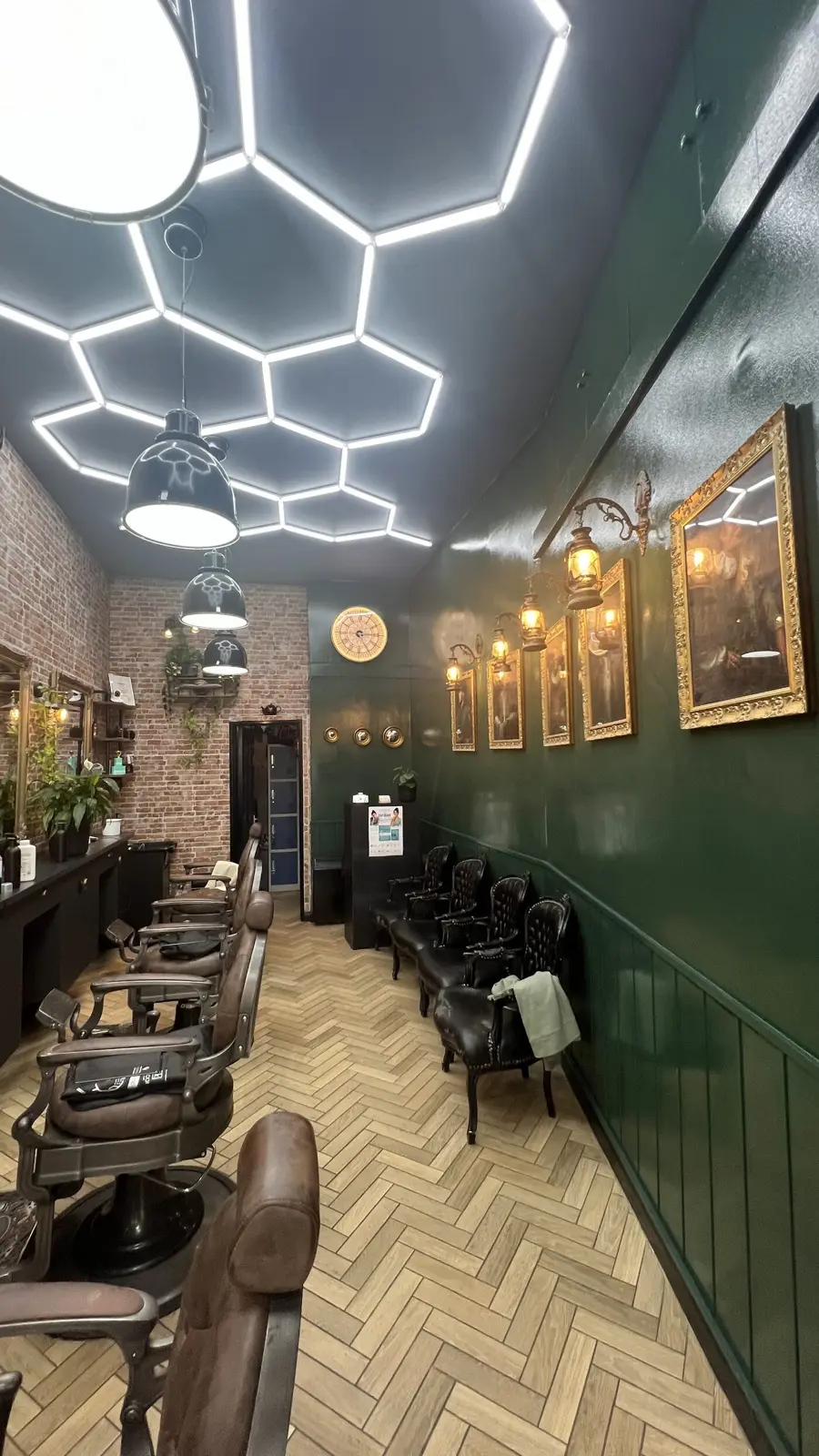 Inside Cut & Go: bottle-green panelled walls, brass lamps, gilt frames and a row of barber chairs under a honeycomb light ceiling